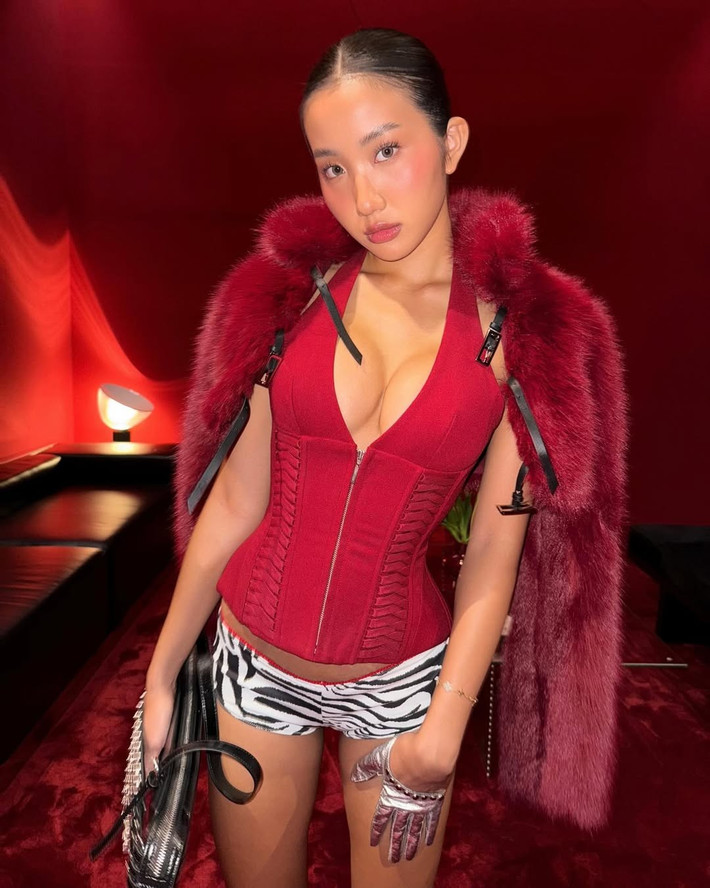 Với outfit đầu tiên, cô nàng diện áo corset màu đỏ rực rỡ với phần cổ yếm xẻ sâu, khoe trọn vòng một gợi cảm và bờ vai thon thả. Chiếc áo được phối cùng quần shorts họa tiết da ngựa vằn, tạo sự tương phản thú vị và tăng thêm vẻ cá tính.
