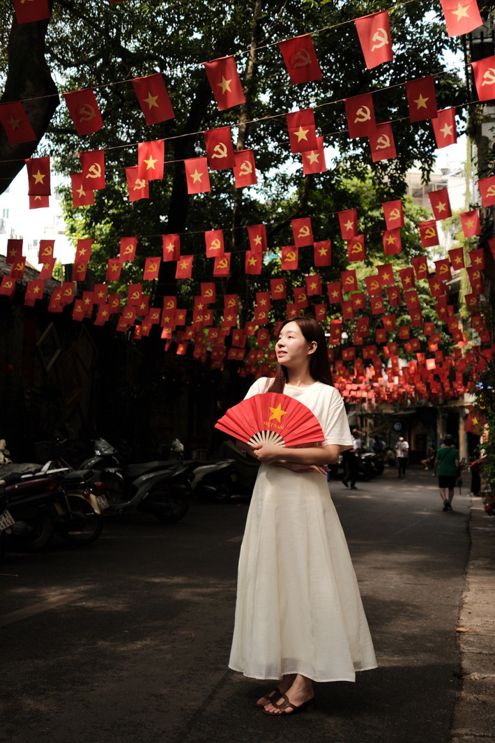 Trong bộ ảnh, cặp đôi MC cùng nhau tạo dáng giữa con phố rực rỡ sắc đỏ của hàng trăm lá cờ Đảng và cờ Tổ quốc. (Ảnh: FB Gia Đình Truyền Hình)