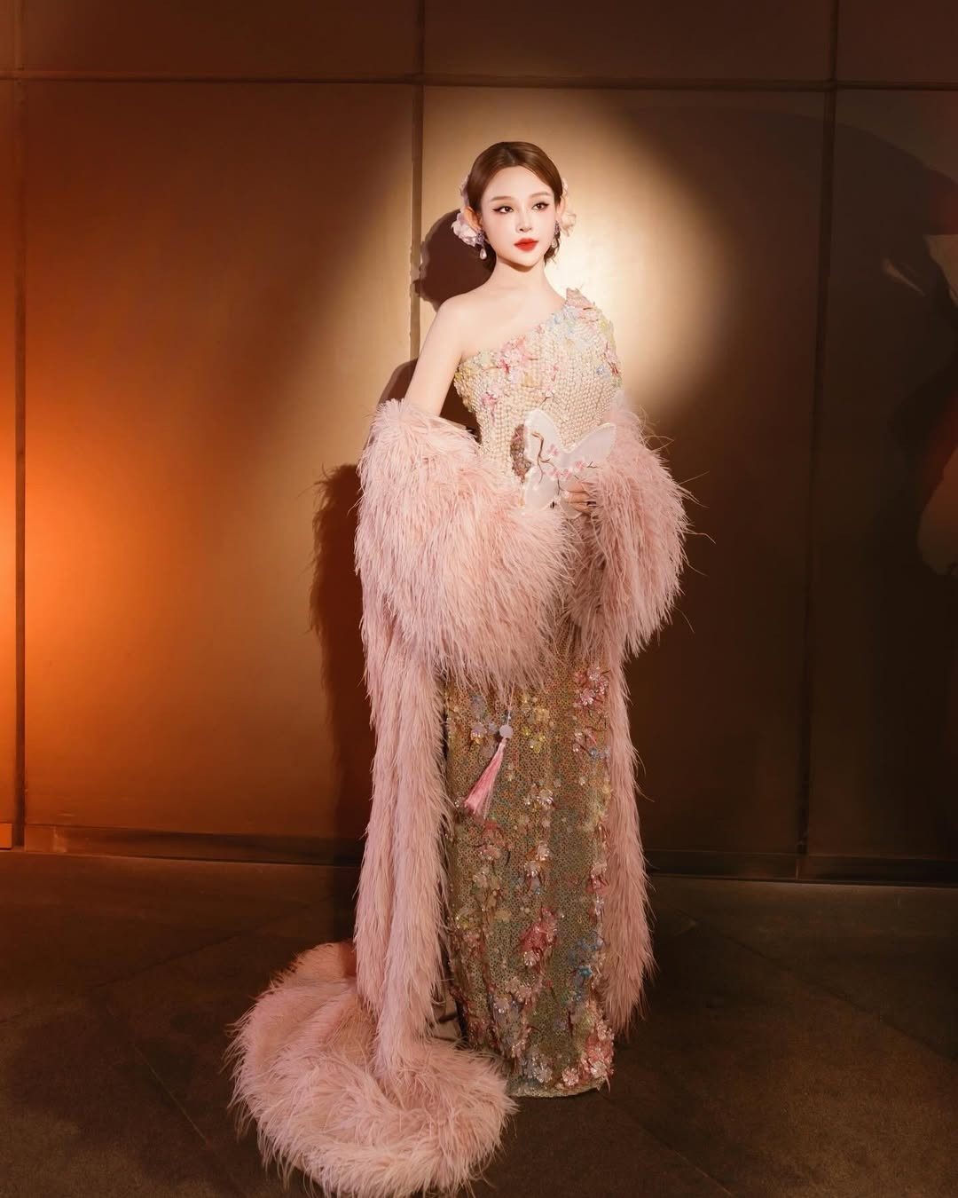 Điểm nhấn đắt giá nhất chính là chiếc khăn choàng lông vũ màu hồng pastel khổng lồ. Chiếc khăn không chỉ tạo độ bồng bềnh, quyền lực mà còn kéo dài thành đuôi váy quét đất, giúp mỗi bước đi của "chị đẹp" trên thảm đỏ trở nên uyển chuyển và thu hút hơn bao giờ hết. (Ảnh: IGNV)