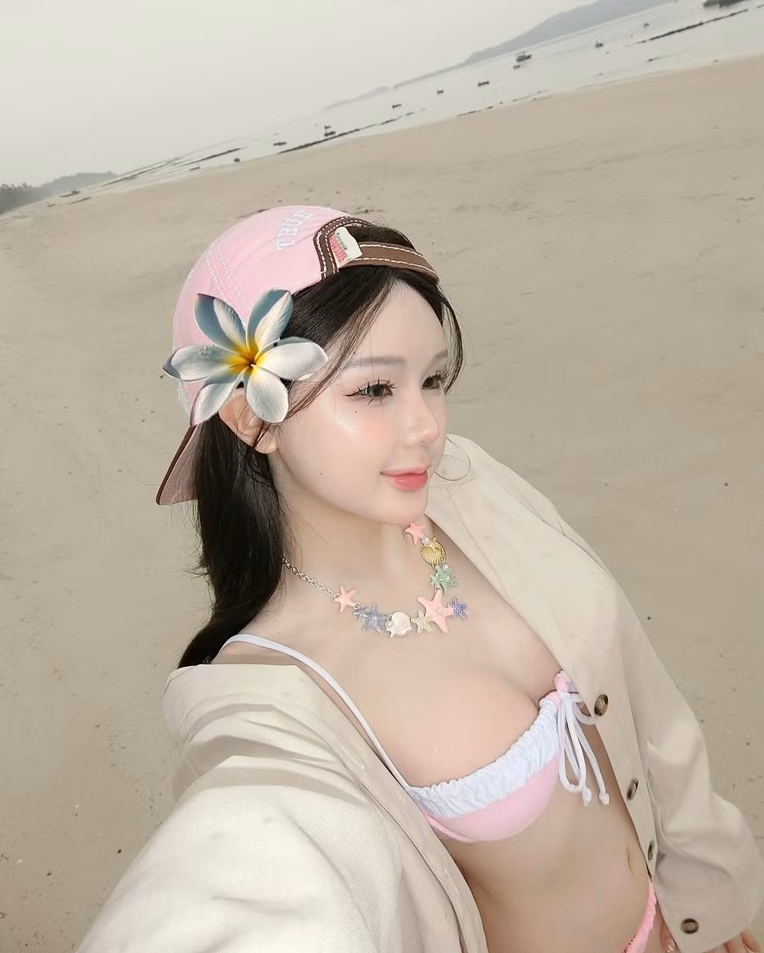 Cô nàng kết hợp bikini cùng mũ lưỡi trai hồng pastel đội ngược, tạo nên sự tương phản thú vị giữa sự nữ tính và cá tính.