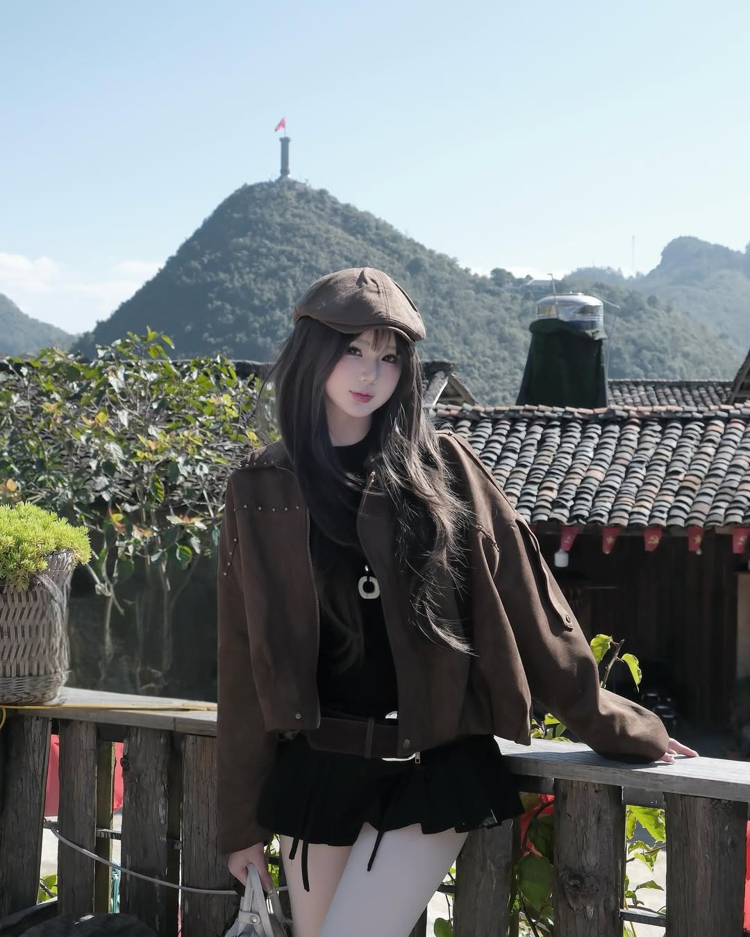 Từ ban công nhà nghỉ hay quán cà phê trong bản, Cột cờ Lũng Cú sừng sững trên đỉnh núi Rồng luôn là phông nền tự hào và hùng vĩ nhất. Hạnh Nguyễn đã ghi lại khoảnh khắc ấn tượng này trong khung cảnh nhà trình tường lợp ngói âm dương truyền thống. (Ảnh: IGNV)