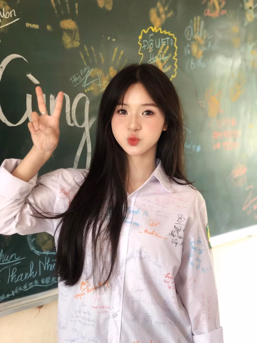 Trong những bức ảnh được lan truyền, nữ sinh xuất hiện trong bộ đồng phục trắng truyền thống – chiếc áo sơ mi lưu bút đã kín đầy chữ ký bạn bè, đứng trước bảng đen với những dấu tay, chữ viết và lời nhắn gửi đáng yêu của tuổi học trò.