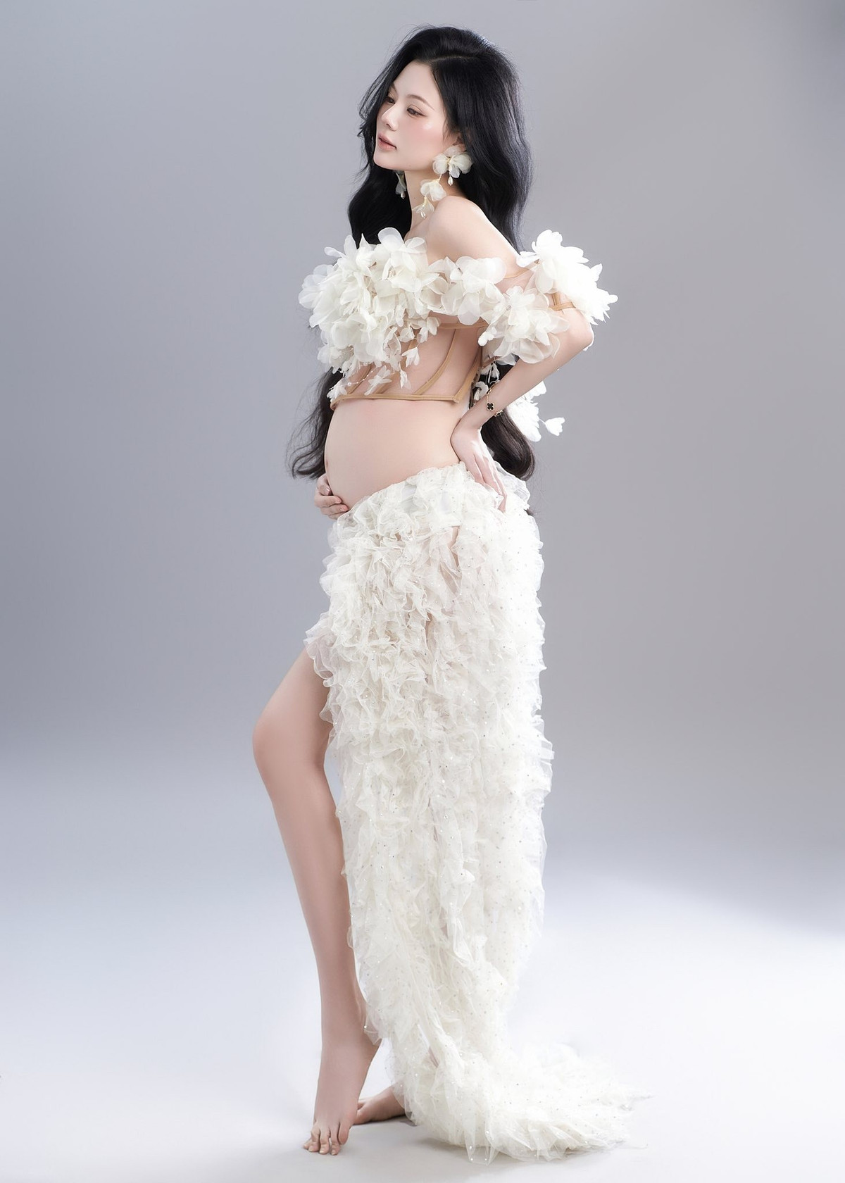 Ngoài ra, Linh Chi cũng thực hiện một bộ ảnh bầu khác với concept hoa trắng nhẹ nhàng, thơ mộng. Cô chọn trang phục với chi chi tiết ren trắng tinh khôi, khoe khéo đường cong cơ thể và bụng bầu một cách nghệ thuật, toát lên vẻ đẹp dịu dàng của người mẹ. (Ảnh: FBNV)