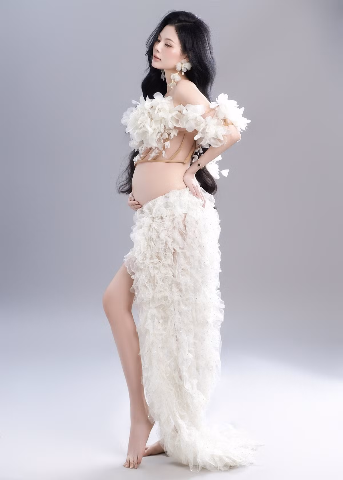 Ngoài ra, Linh Chi cũng thực hiện một bộ ảnh bầu khác với concept hoa trắng nhẹ nhàng, thơ mộng. Cô chọn trang phục với chi chi tiết ren trắng tinh khôi, khoe khéo đường cong cơ thể và bụng bầu một cách nghệ thuật, toát lên vẻ đẹp dịu dàng của người mẹ. (Ảnh: FBNV)