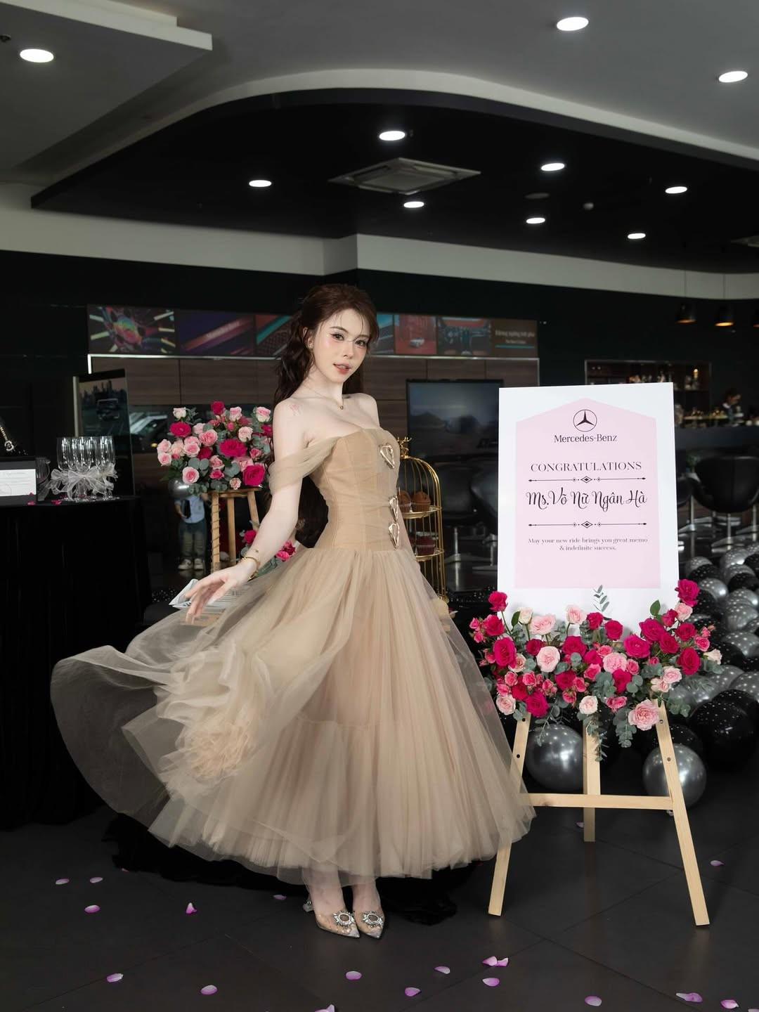 Ngân Hà tự tin tạo dáng bên chiếc Mercedes-Benz màu trắng, với bó hoa hồng đỏ rực và những quả bóng bay hình trái tim lấp lánh, tạo nên một khung cảnh chúc mừng đầy lãng mạn và sang trọng.