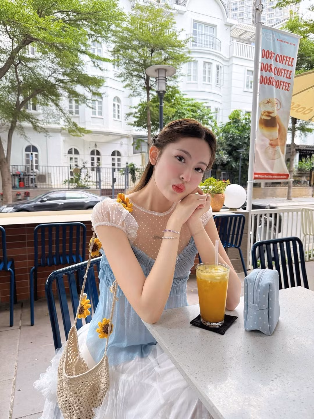 Điểm nhấn của trang phục là chi tiết bèo nhún tinh tế cùng những bông hoa nhỏ xinh được cài trên vai và túi xách, càng làm tăng thêm vẻ đáng yêu và dịu dàng.