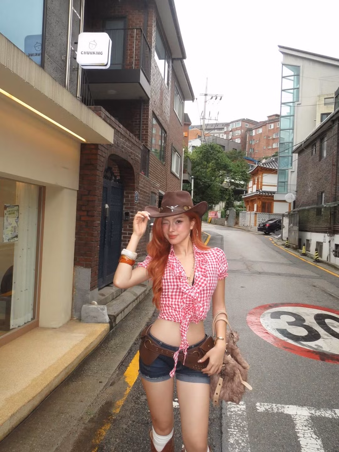 Quần short jeans ngắn năng động, kết hợp với thắt lưng bản to và chiếc túi đeo hông da nâu đậm chất cao bồi. (Ảnh: IGNV)