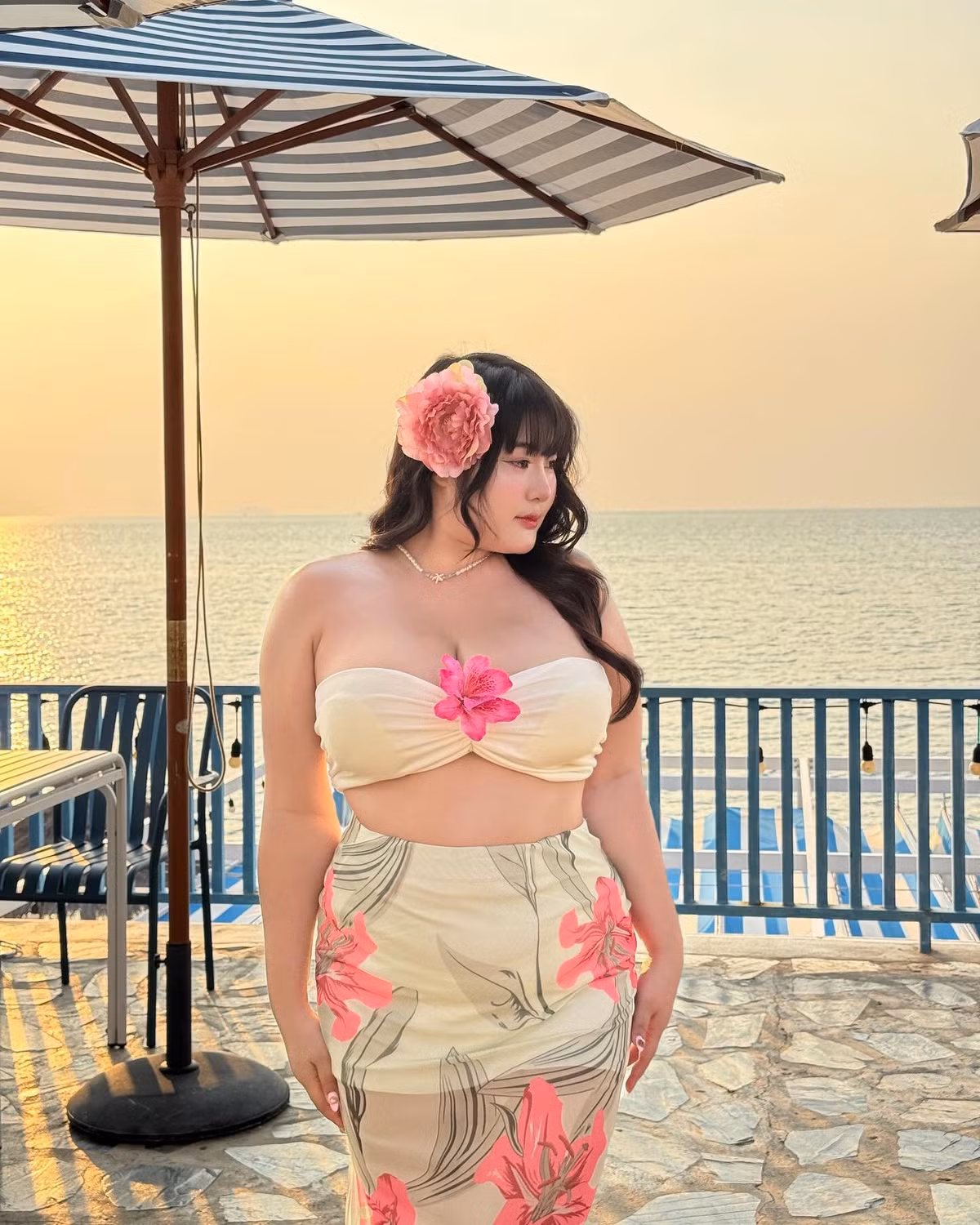 Điểm nhấn là đóa hoa cài tóc và bông hoa nổi bật giữa ngực, vừa nữ tính vừa tôn lên thần thái quyến rũ.