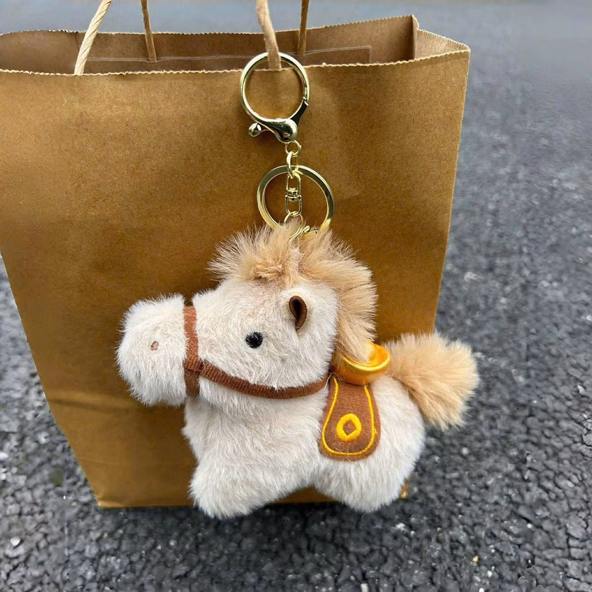 Những chiếc móc khóa bông được làm từ lông mịn cao cấp với các tông màu như trắng kem, nâu nhạt hoặc đỏ rực rỡ. Điểm nhấn là chiếc yên ngựa thêu tay tinh xảo cùng hình thỏi vàng nhỏ xinh trên lưng.