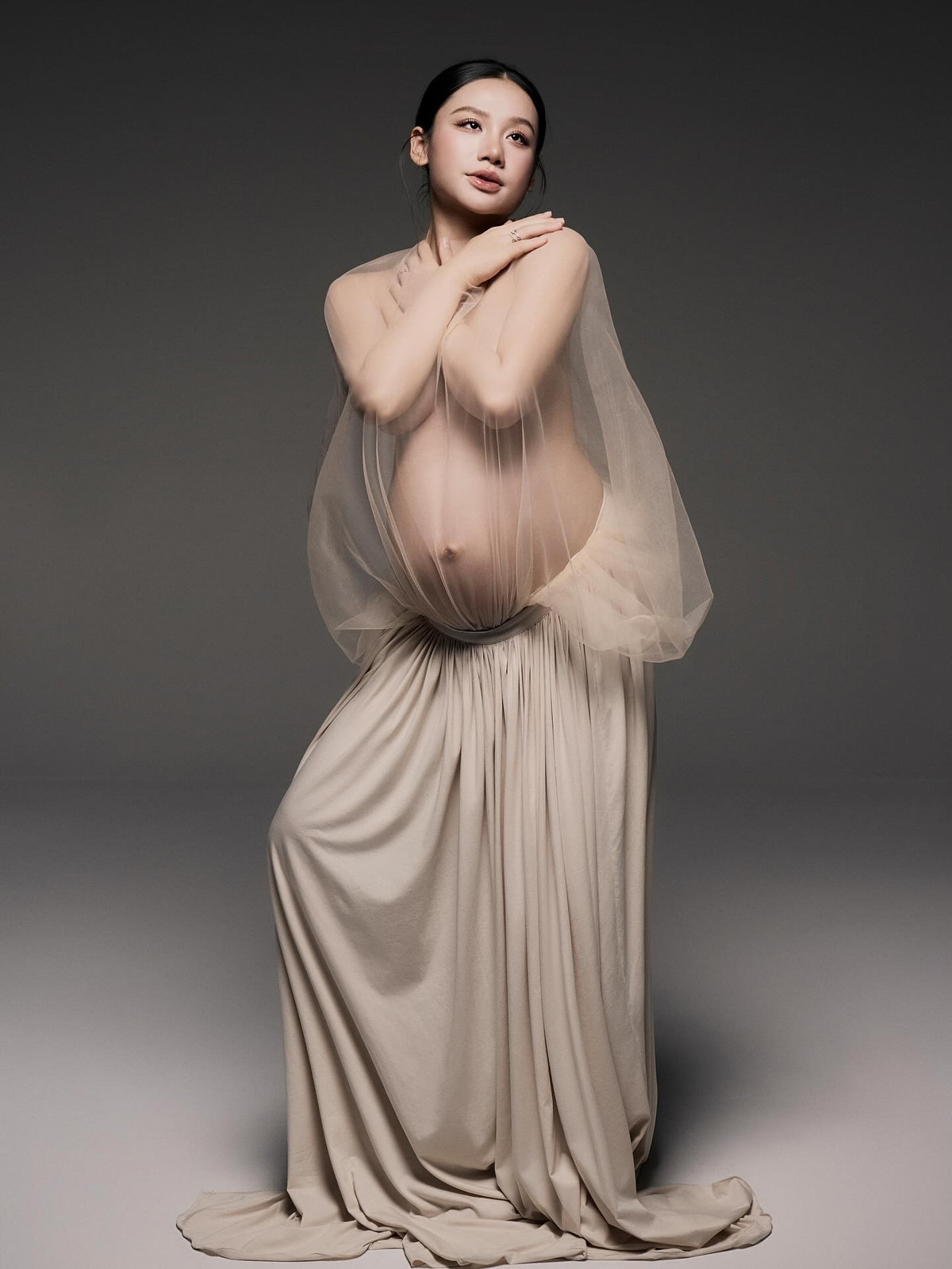 Trong bộ ảnh, Minh Thư diện trang phục đơn giản với một chiếc váy dài xếp ly màu be nhạt kết hợp với lớp vải voan mỏng manh phủ hờ hững phần thân trên. (Ảnh: FBNV)