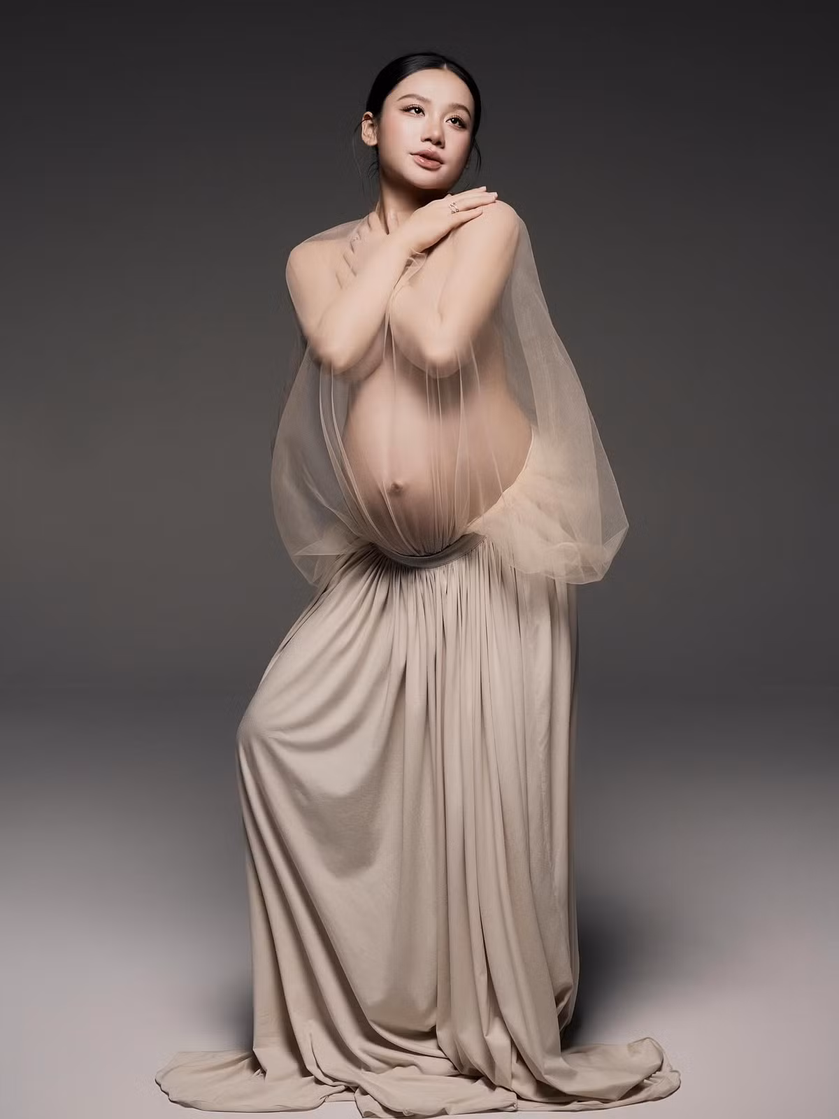 Trong bộ ảnh, Minh Thư diện trang phục đơn giản với một chiếc váy dài xếp ly màu be nhạt kết hợp với lớp vải voan mỏng manh phủ hờ hững phần thân trên. (Ảnh: FBNV)