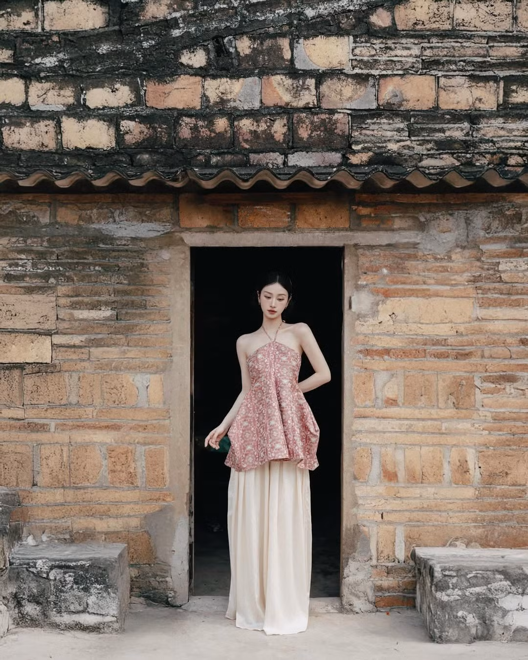 Sự đồng điệu giữa màu sắc đỏ trầm cùng những hoa văn trên chiếc áo yếm với kiến trúc gạch đỏ khiến bộ ảnh càng thêm đậm chất hoài cổ, xưa cũ. (Ảnh: IGNV)