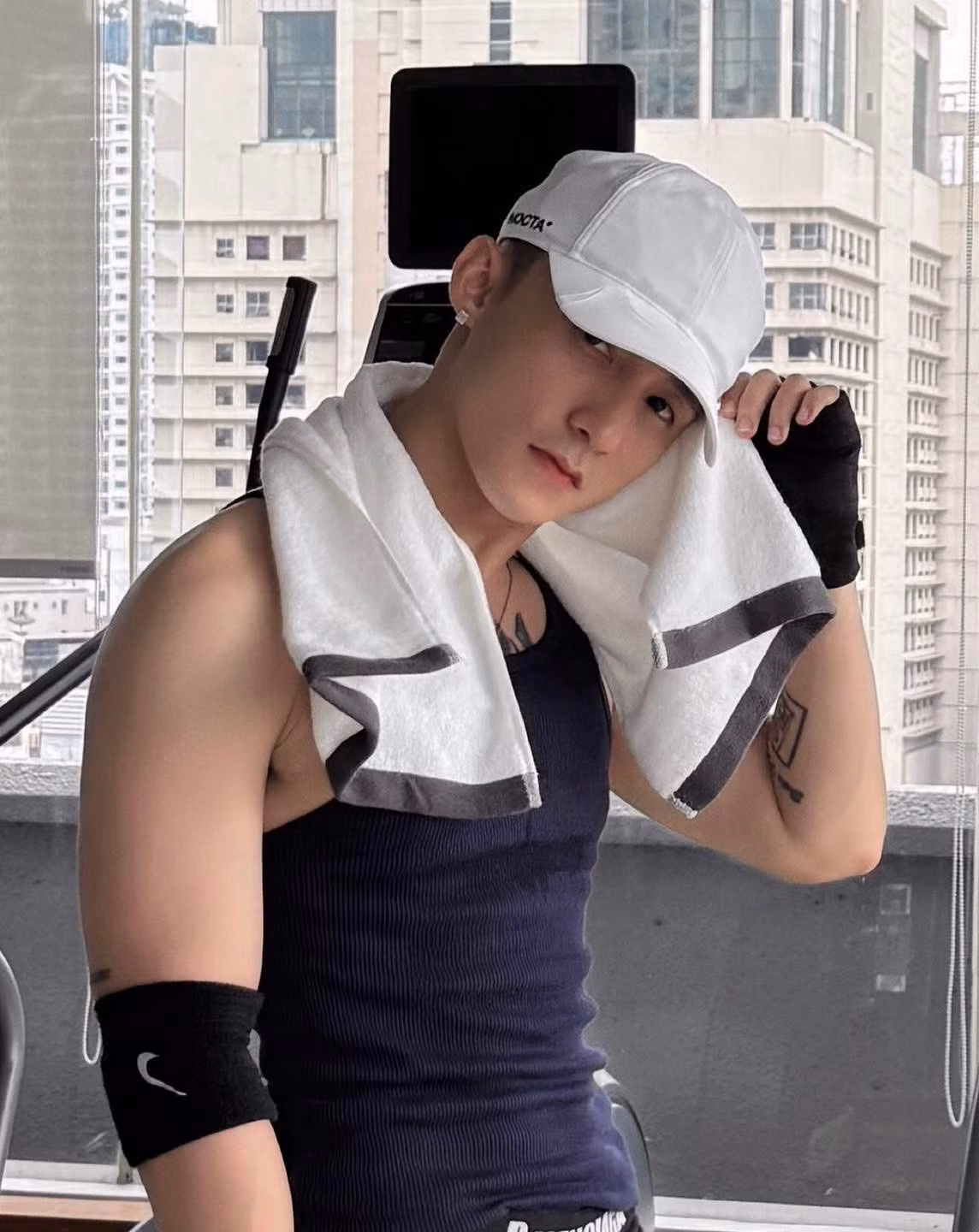 Điểm nhấn mạnh mẽ nhất chính là đôi giày thể thao màu cam neon cực kỳ nổi bật. Chiếc mũ lưỡi trai và găng tay tập gym không chỉ là phụ kiện mà còn hoàn thiện phong cách thể thao, bụi bặm đầy cuốn hút.