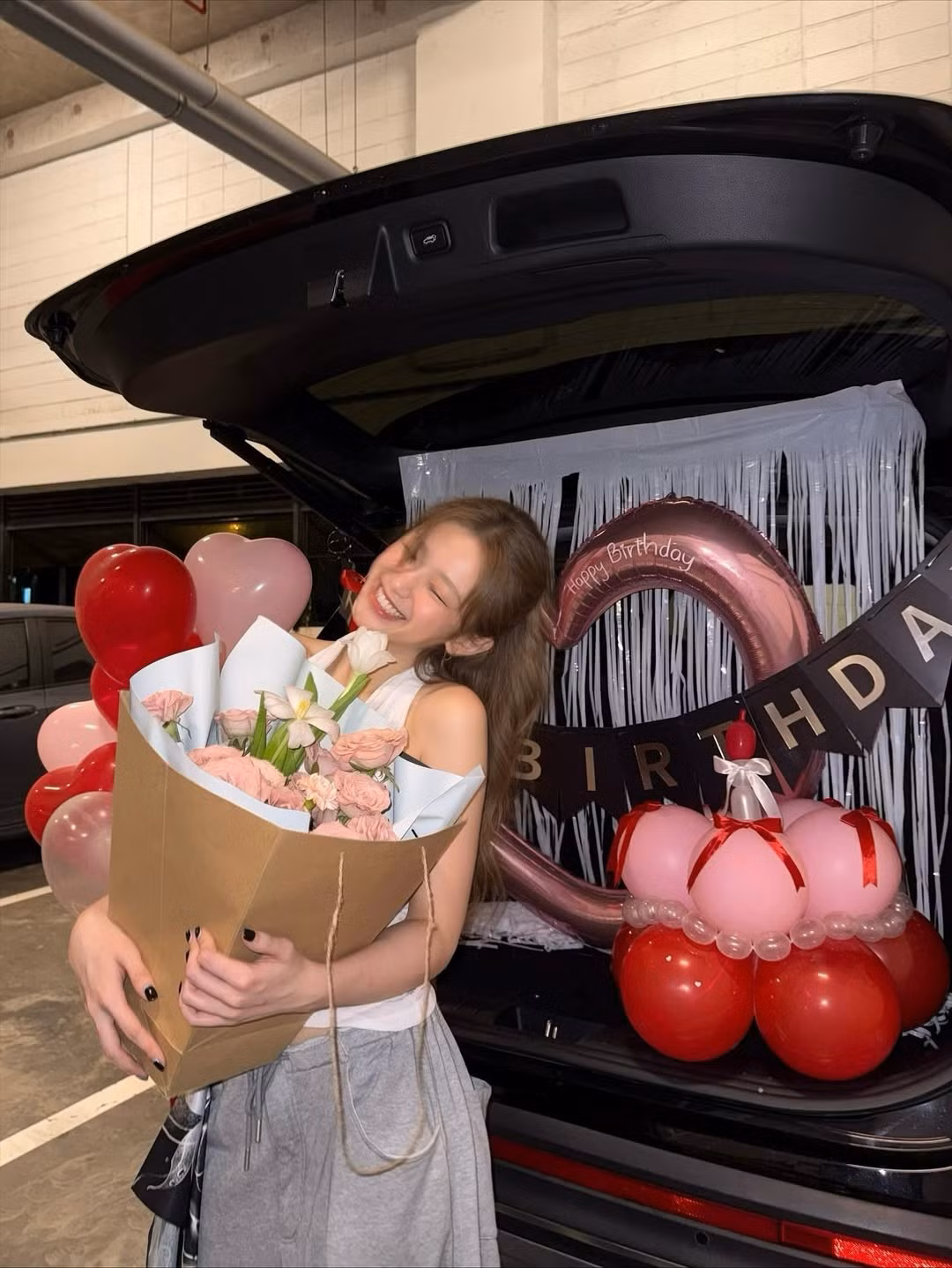 Tiệc sinh nhật được trang trí lãng mạn ở khoang sau xe ô tô, với bóng bay hình trái tim màu đỏ. Linh Ka nhận được một bó hoa lớn với sắc hồng nhẹ nhàng. Cô mỉm cười rạng rỡ, khoảnh khắc đón tuổi mới ngập tràn niềm vui và sự ngọt ngào (Ảnh: FBNV)