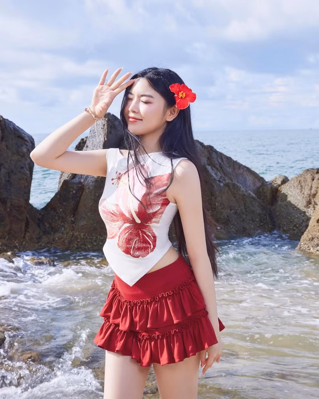 Để hoàn thiện tổng thể, cô nàng không quên cài một bông hoa đỏ trên tóc - chi tiết nhỏ nhưng vô cùng tinh tế, tạo sự hài hòa với tông màu chủ đạo của outfit. Mái tóc dài buông xõa tự nhiên càng làm tôn lên vẻ đẹp trong trẻo của con gái MC nổi tiếng.