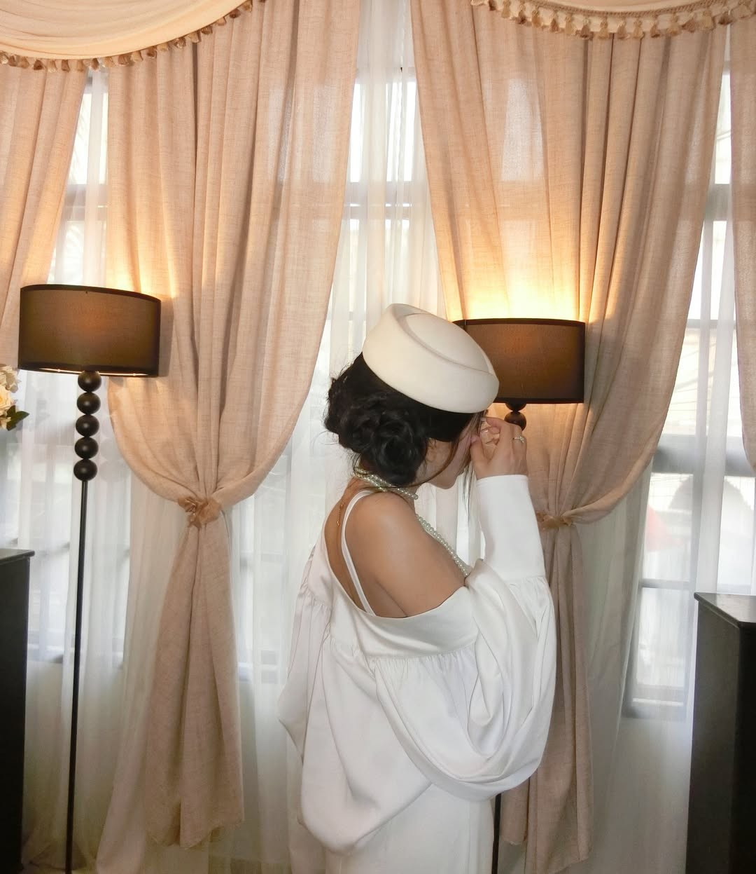 Dưới ánh đèn vàng ấm áp của không gian nội thất sang trọng, Mai Dora không cần tạo dáng quá cầu kỳ. Dù là khi e ấp bên bó hoa hồng trắng hay lặng lẽ ngắm nhìn những bức tranh nghệ thuật, mỗi khung hình đều toát lên sự tĩnh lặng, quý phái và vô cùng cuốn hút. (Ảnh: IGNV)