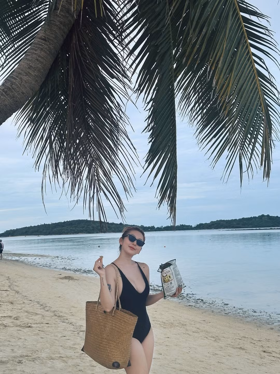 Cô nàng kết hợp cùng phụ kiện sành điệu là chiếc túi cói bản lớn, kính râm thời trang và tạo dáng dưới bóng mát của hàng dừa. (Ảnh: IGNV)