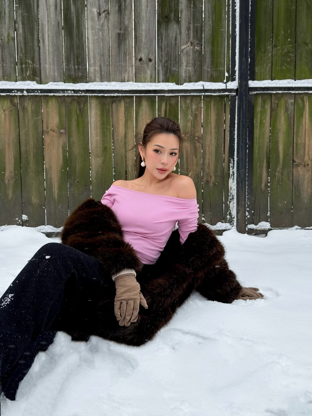 Giữa khung cảnh tuyết rơi dày đặc, Nguyên Newin xuất hiện đầy ấn tượng trong trang phục mang tông hồng pastel và nâu trầm chủ đạo. Cô nàng khéo léo lựa chọn chiếc áo trễ vai màu hồng dịu mắt, giúp tôn lên bờ vai thon thả và làn da trắng ngần. (Ảnh: IGNV)