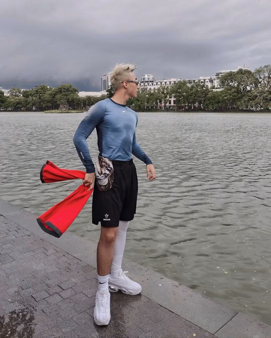 Nam ca sĩ diện trang phục thể thao với áo thun dài tay màu xanh xám, quần short đen, cùng phụ kiện là tất và giày thể thao trắng. Anh còn khoác hờ chiếc khăn màu đỏ nổi bật, tạo điểm nhấn rực rỡ trên nền trời âm u của Hà Nội.