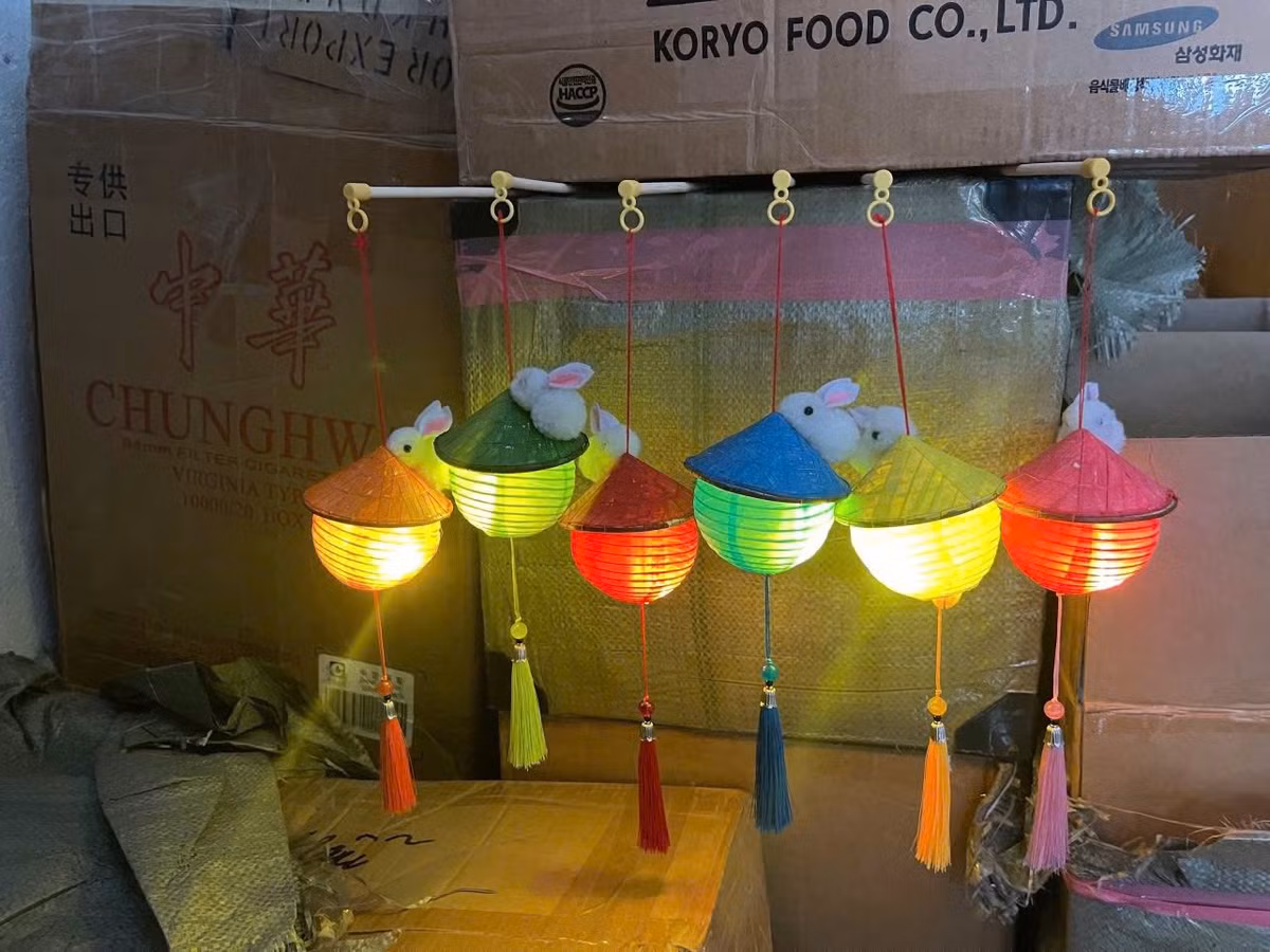 Cụ thể, phần chao đèn được làm thành hình nón, phối màu rực rỡ với họa tiết cờ Việt Nam, có khi còn gắn thêm thú bông nhỏ xinh như thỏ trắng