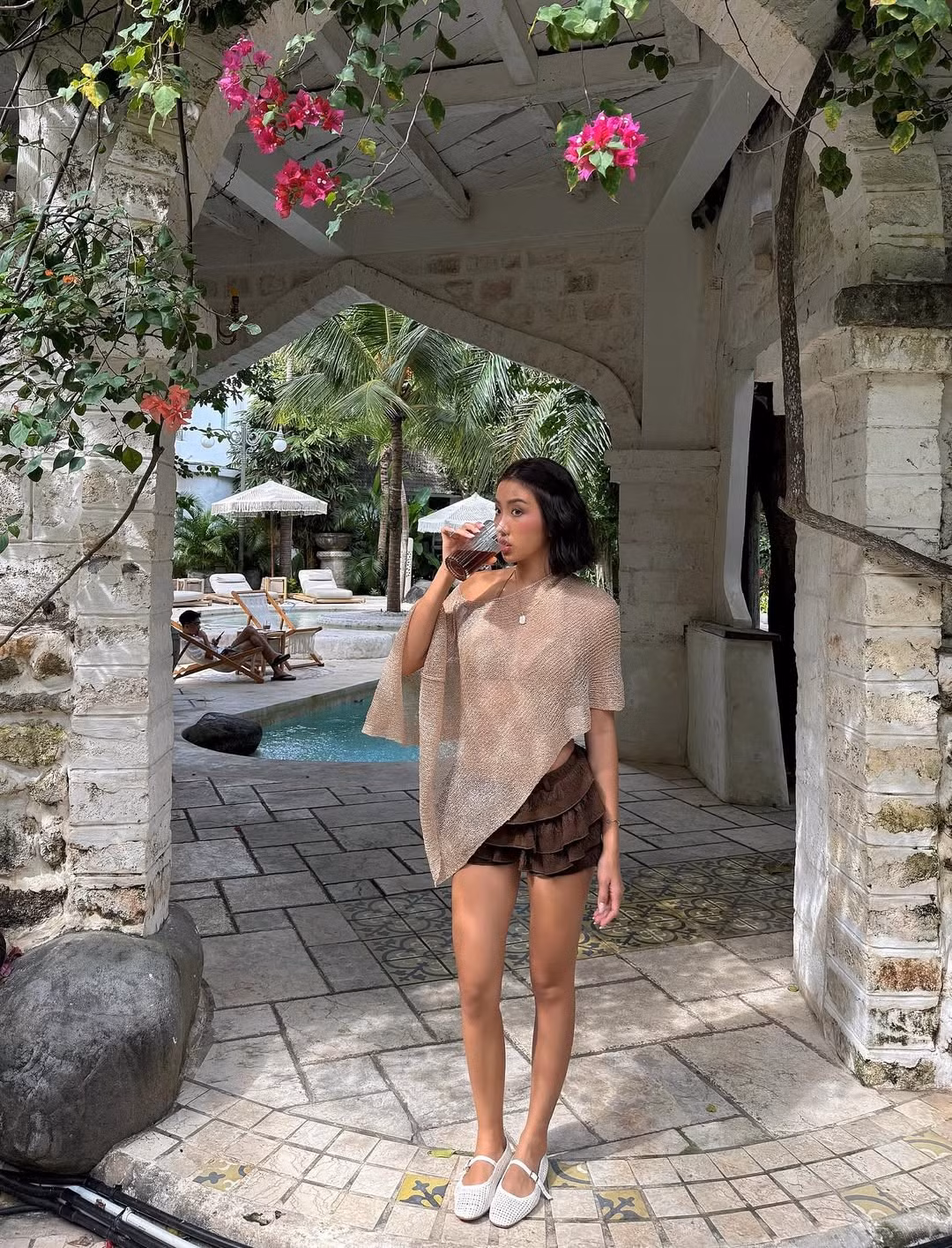 Ở những khung hình khác, cô nàng diện chiếc áo poncho mỏng màu be độc đáo, kết hợp cùng quần short nâu xếp tầng và đôi giày bệt trắng thoải mái.