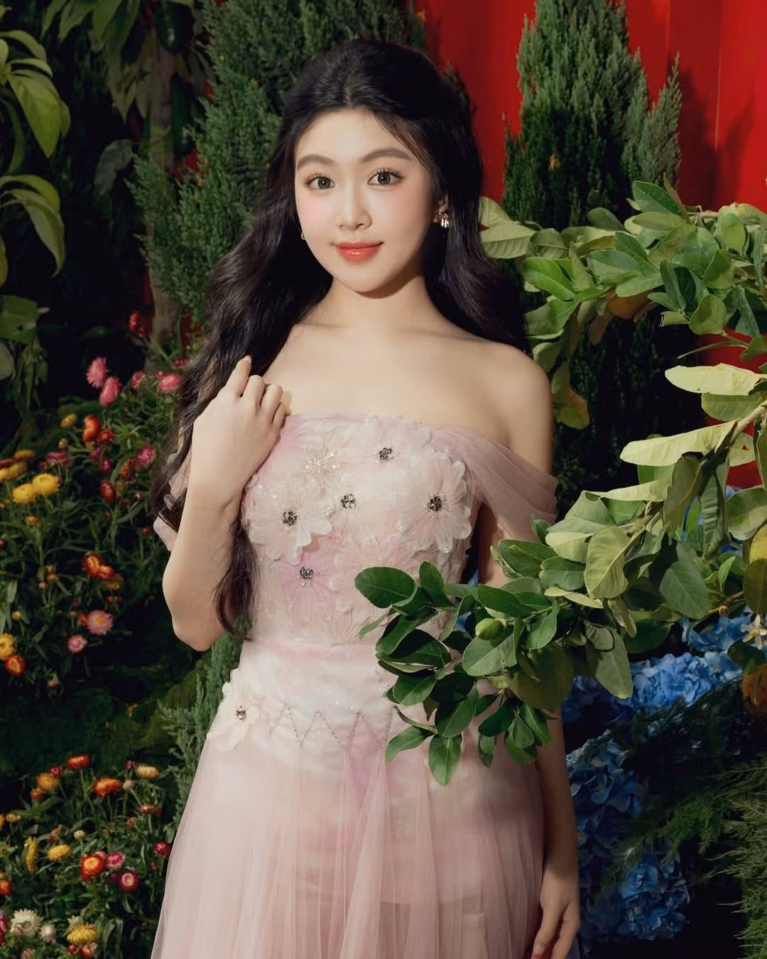 Cô nàng khoác lên mình chiếc váy dạ hội màu hồng pastel nhẹ nhàng, với thiết kế tinh tế. Phần thân trên được đính kết những cánh hoa 3D mềm mại, kết hợp cùng chi tiết trễ vai hờ hững, khoe khéo bờ vai thon thả.