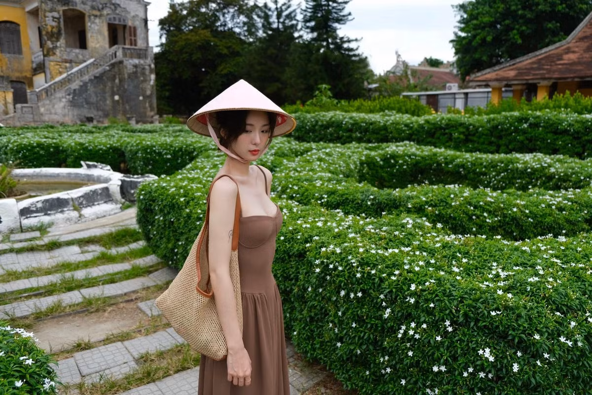 Điểm nhấn không thể thiếu là chiếc nón lá truyền thống, che hờ gương mặt thanh tú, tạo nên vẻ đẹp bí ẩn và đầy chất thơ.
