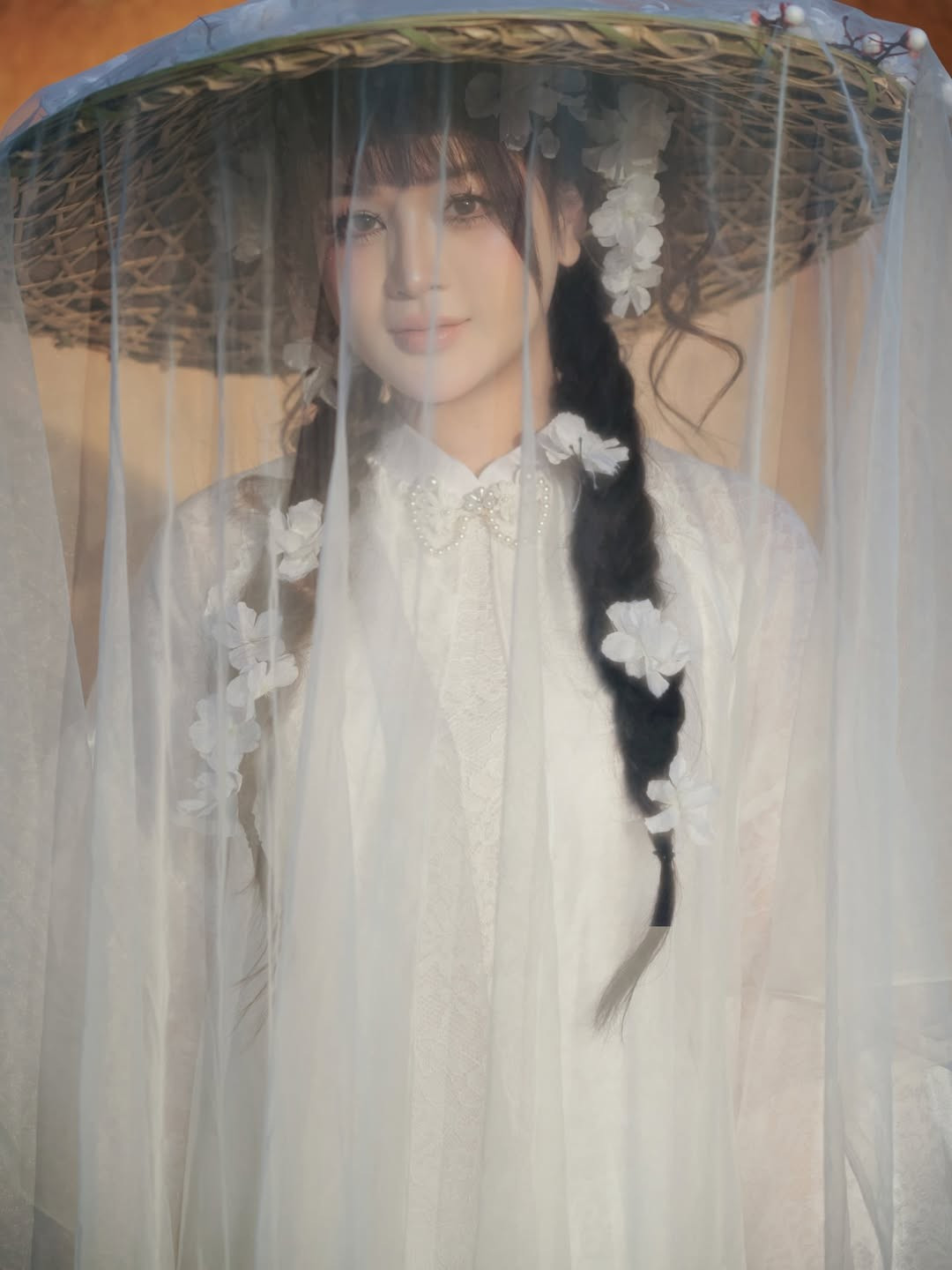 Hình ảnh Lyly Sury đội chiếc nón lá gắn dải voan mỏng và hoa trắng là khoảnh khắc đắt giá nhất. Nó không chỉ là món phụ kiện truyền thống mà còn tạo nên hiệu ứng "mờ ảo", tăng thêm phần bí ẩn và cuốn hút cho gương mặt. (Ảnh: IGNV)