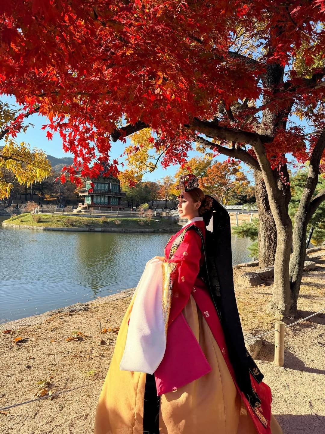 Trang phục nổi bật với áo jeogori và váy chima màu đỏ rực rỡ, kết hợp hài hòa cùng các chi tiết màu trắng, đen và vàng đồng. Màu đỏ thêu hoa văn phức tạp và đường viền vàng lấp lánh càng làm tăng thêm vẻ quyền quý. (Ảnh: IGNV)