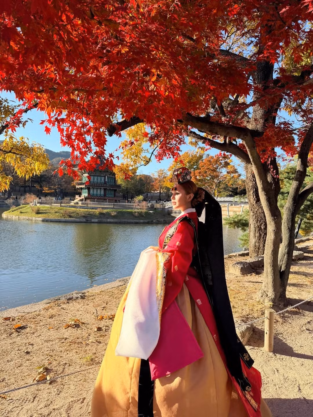 Trang phục nổi bật với áo jeogori và váy chima màu đỏ rực rỡ, kết hợp hài hòa cùng các chi tiết màu trắng, đen và vàng đồng. Màu đỏ thêu hoa văn phức tạp và đường viền vàng lấp lánh càng làm tăng thêm vẻ quyền quý. (Ảnh: IGNV)