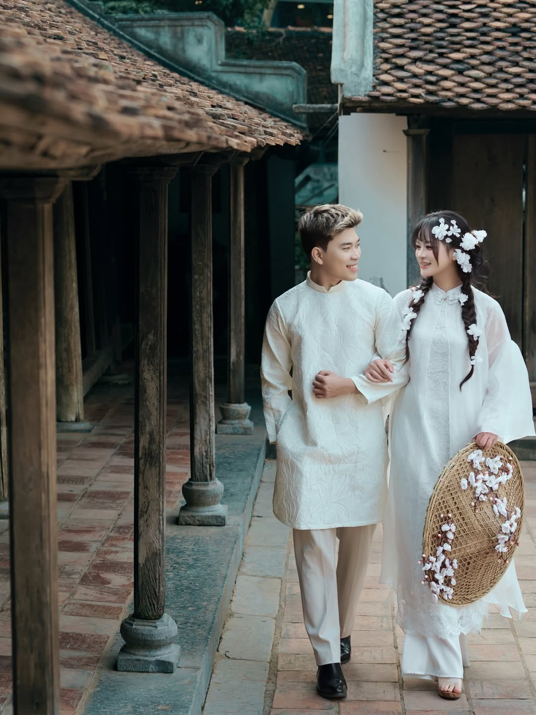 Cặp đôi lựa chọn tông màu trắng kem và trắng tinh khôi làm chủ đạo. Lyly Sury diện thiết kế áo dài cách tân nhiều lớp với chất liệu tơ mỏng nhẹ, điểm xuyết những bông hoa nhỏ dọc theo tà áo và mái tóc tết điệu đà. (Ảnh: IGNV)