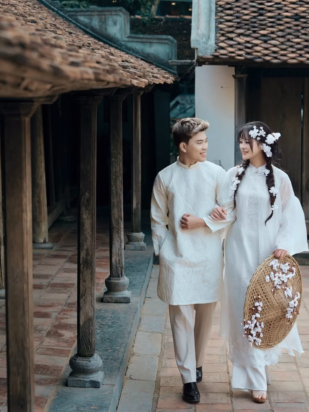 Cặp đôi lựa chọn tông màu trắng kem và trắng tinh khôi làm chủ đạo. Lyly Sury diện thiết kế áo dài cách tân nhiều lớp với chất liệu tơ mỏng nhẹ, điểm xuyết những bông hoa nhỏ dọc theo tà áo và mái tóc tết điệu đà. (Ảnh: IGNV)