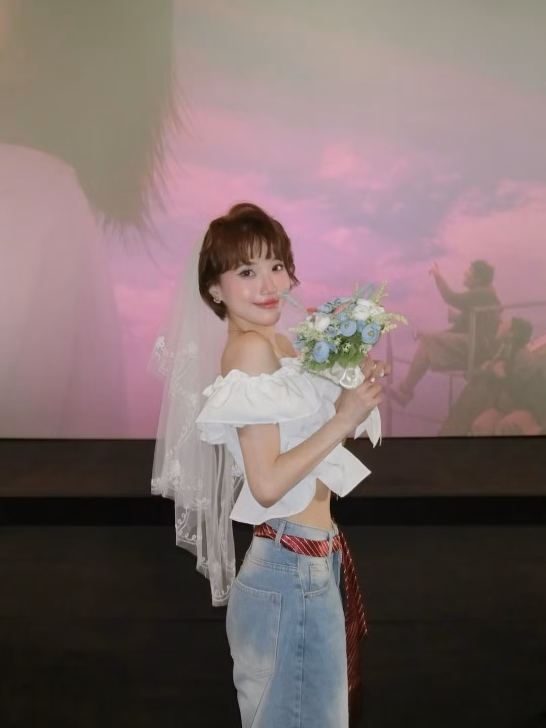 Cô nàng diện áo trắng trễ vai, đội voan cưới , tay cầm hoa cô dâu. (Ảnh: IG @feifeikhanh)