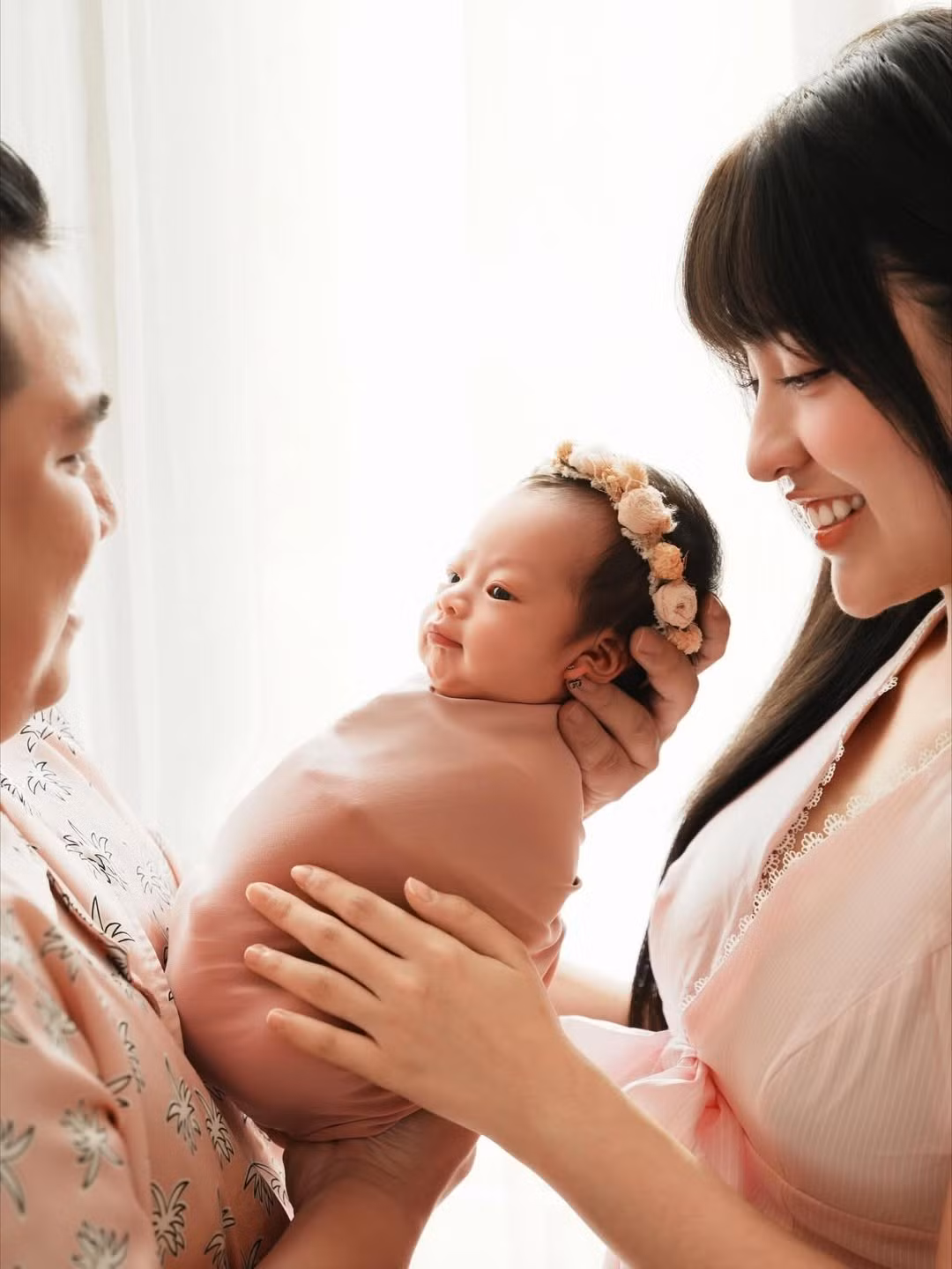 Hình ảnh bố mẹ nhìn nhau, cùng nhau nâng niu thiên thần nhỏ với ánh mắt trìu mến đã khắc họa rõ nét niềm hạnh phúc và sự gắn kết của gia đình. (Ảnh: IGNV)