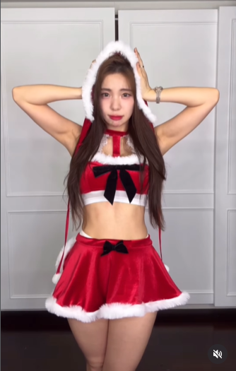 Trong set đồ đầu tiên, Lee Da Hye diện crop top và chân váy màu đỏ nhung với viền lông trắng. Thiết kế hở eo và chi tiết nơ đen lớn giúp cô khoe trọn vòng eo chỉ 56cm "siêu thực" đã làm nên thương hiệu. Mũ trùm đầu Noel đi kèm càng làm tăng thêm vẻ đáng yêu, tinh nghịch.