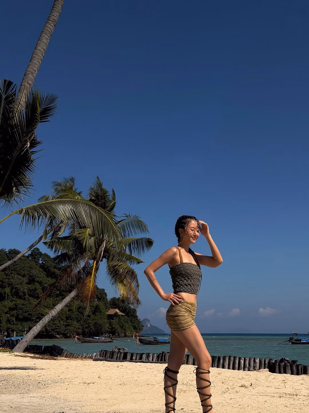 Người đẹp diện một set đồ crop top và chân váy mini màu xanh rêu - vàng đồng ton sur ton. Bộ trang phục đặc biệt với chất liệu và họa tiết dệt, đan thủ công, tạo cảm giác gần gũi với thiên nhiên, hòa hợp tuyệt đối với khung cảnh biển xanh nắng vàng. (Ảnh: IGNV)