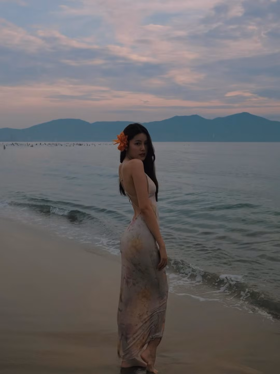 Cô nàng còn cài thêm một bông hoa màu cam rực rỡ lên tóc, tạo điểm nhấn nổi bật và hài hòa với không khí biển cả.