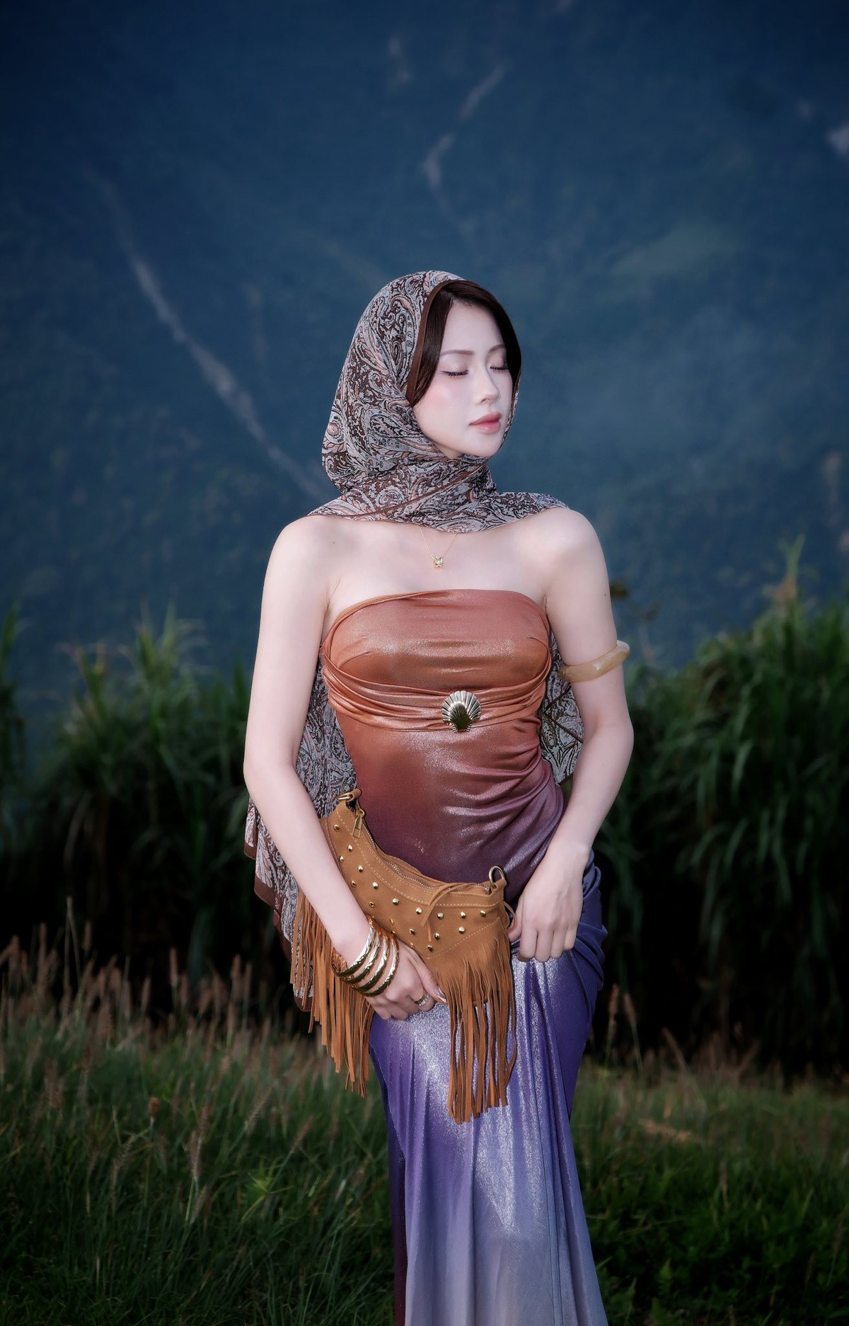 Cô quấn một chiếc khăn họa tiết quanh đầu, mang lại vẻ ngoài bí ẩn, kết hợp cùng chiếc túi xách màu nâu da bò với chi tiết tua rua nổi bật - một phụ kiện kinh điển của phong cách Bohemian. (Ảnh: FBNV)