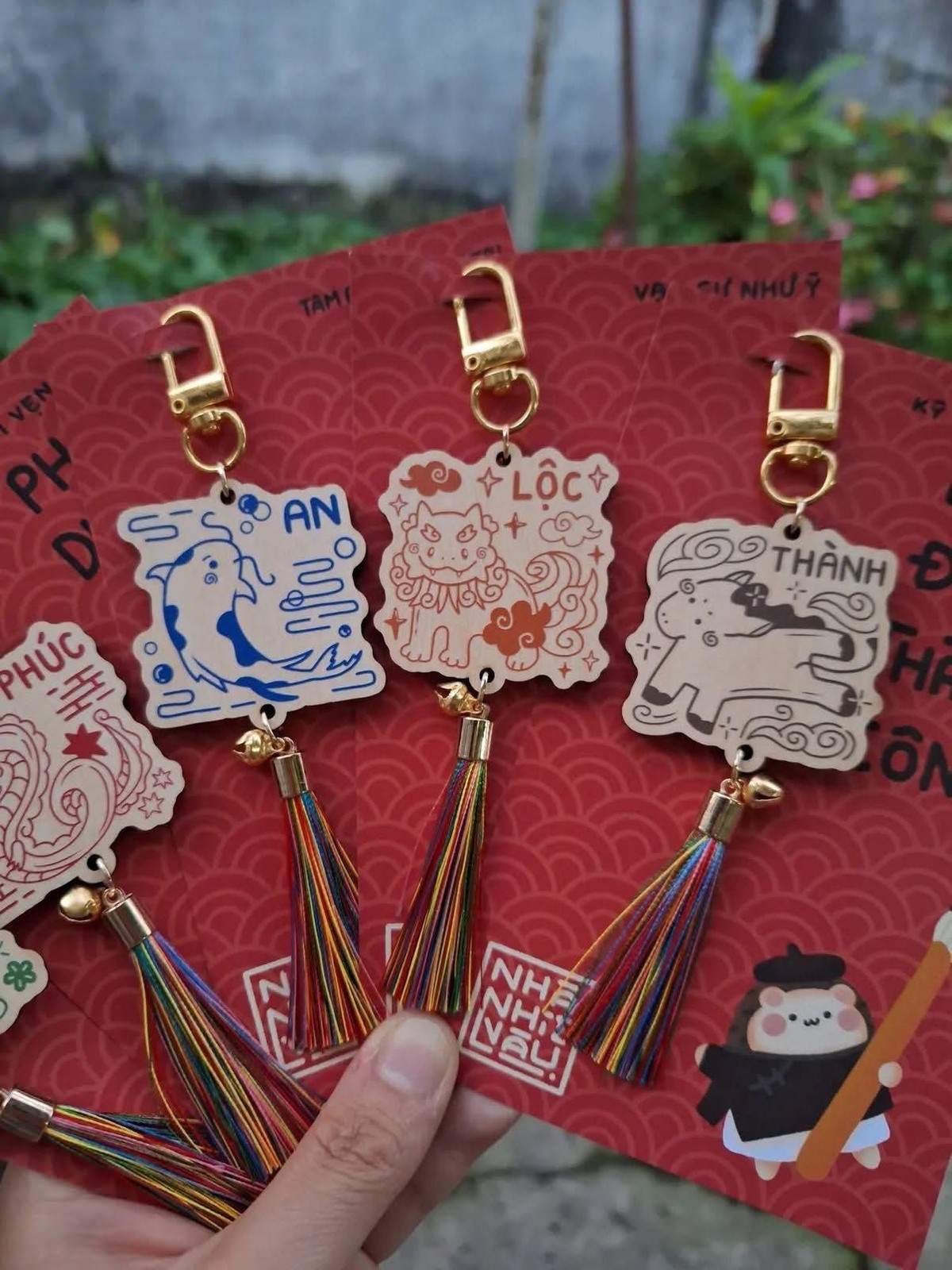 Một sự kết hợp mới lạ năm nay là bao lì xì đi kèm với các móc khóa gỗ hoặc thẻ treo bình an. Trên thẻ có khắc các chữ Hán Việt như An, Lộc, Thành, Nhẫn kèm theo hình ảnh linh vật (Long, Ly, Quy, Phụng hoặc ngựa).