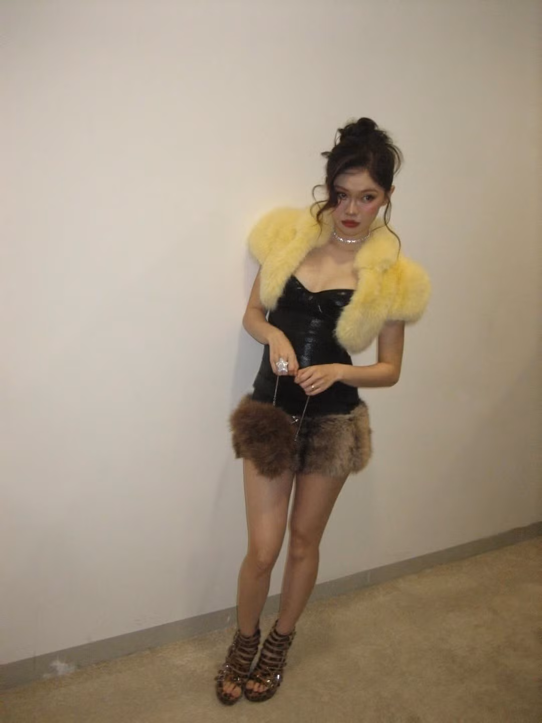 Cùng diện chiếc áo lông dáng lửng màu vàng gà con, thế nhưng Ngọc Trinh chọn cách phối đồ với boots cao cổ da đen và tất đùi, tạo nên vẻ ngoài mạnh mẽ và cá tính. Trong khi đó, Ly Phạm lại chọn sandals cao gót để hoàn thiện tổng thể, mang đến vẻ nữ tính và thanh lịch hơn.