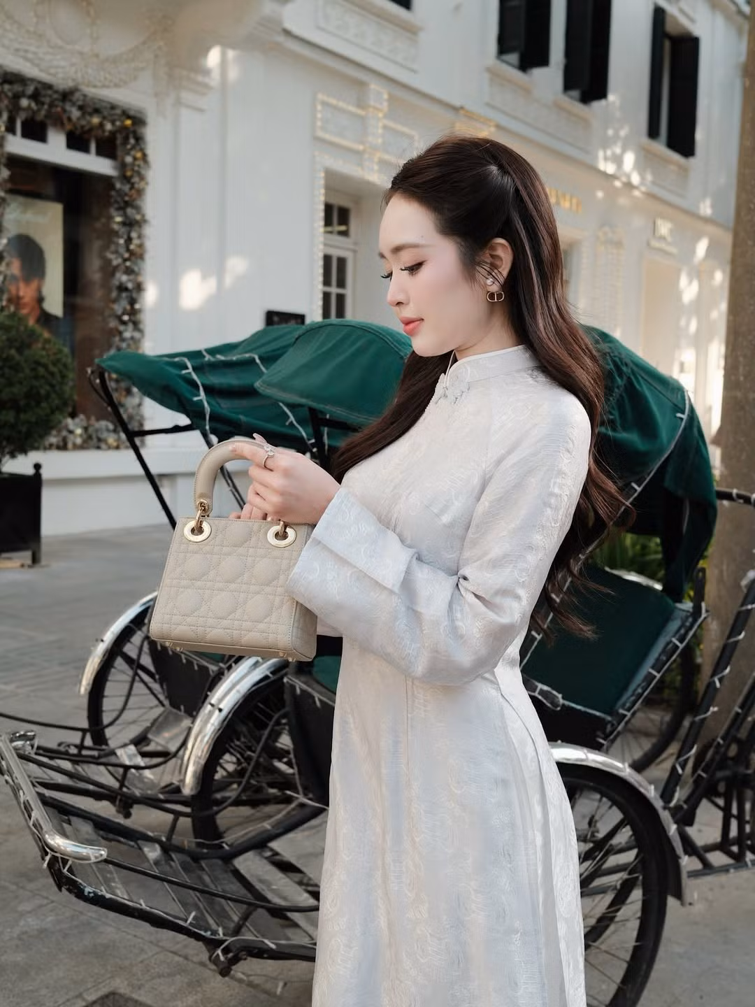 Điểm nhấn thời thượng là chiếc túi xách hàng hiệu cầm tay màu be, nhỏ xinh, tạo nên sự giao thoa độc đáo giữa trang phục truyền thống và phụ kiện hiện đại, khẳng định gu thẩm mỹ tinh tế của hot girl 9X. (Ảnh: IGNV)