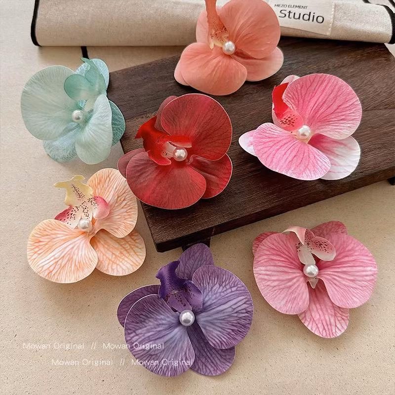 Những mẫu kẹp hoa sứ, hoa lan vốn đã "làm mưa làm gió" những mùa hè năm trước thì năm nay vẫn chưa hề hết hot. Những thiết kế hoa với đủ màu sắc giúp chị em hoàn thiện set đồ, có những tấm ảnh sống ảo đậm chất "nàng thơ".