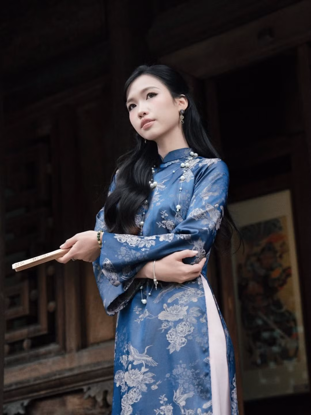 Giữa không gian bảng lảng sương giăng của Hà Nội, Hoàng Minh Ngọc chọn cho mình bộ áo dài gấm tông màu xanh dương đậm, điểm xuyết họa tiết chim hạc và hoa sen in chìm sang trọng. (Ảnh: IGNV)