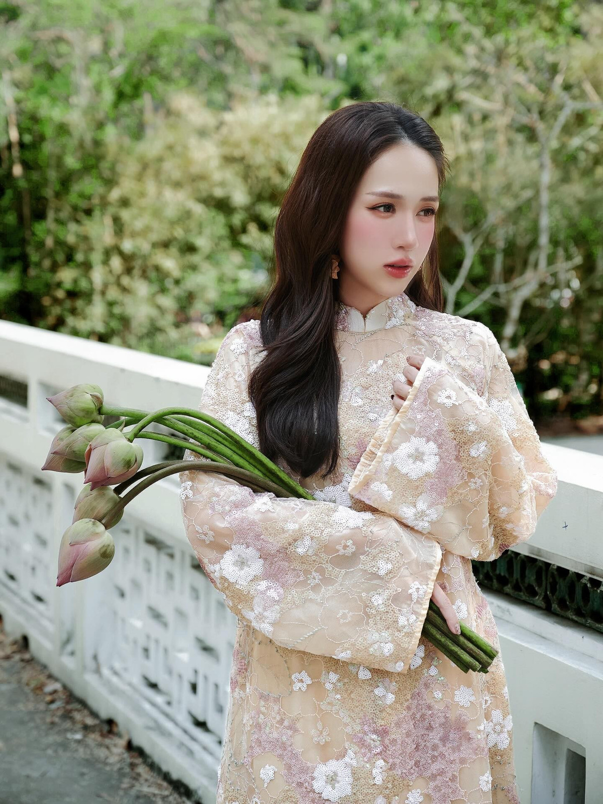 Trên tay Joyce Phạm là những nhành hoa sen hồng đang chớm nở. Sự tương phản giữa sắc hồng của hoa sen và sắc vàng nhạt của tà áo dài tạo nên một tổng thể màu sắc vô cùng hài hòa, đậm chất Việt Nam. (Ảnh: IGNV)