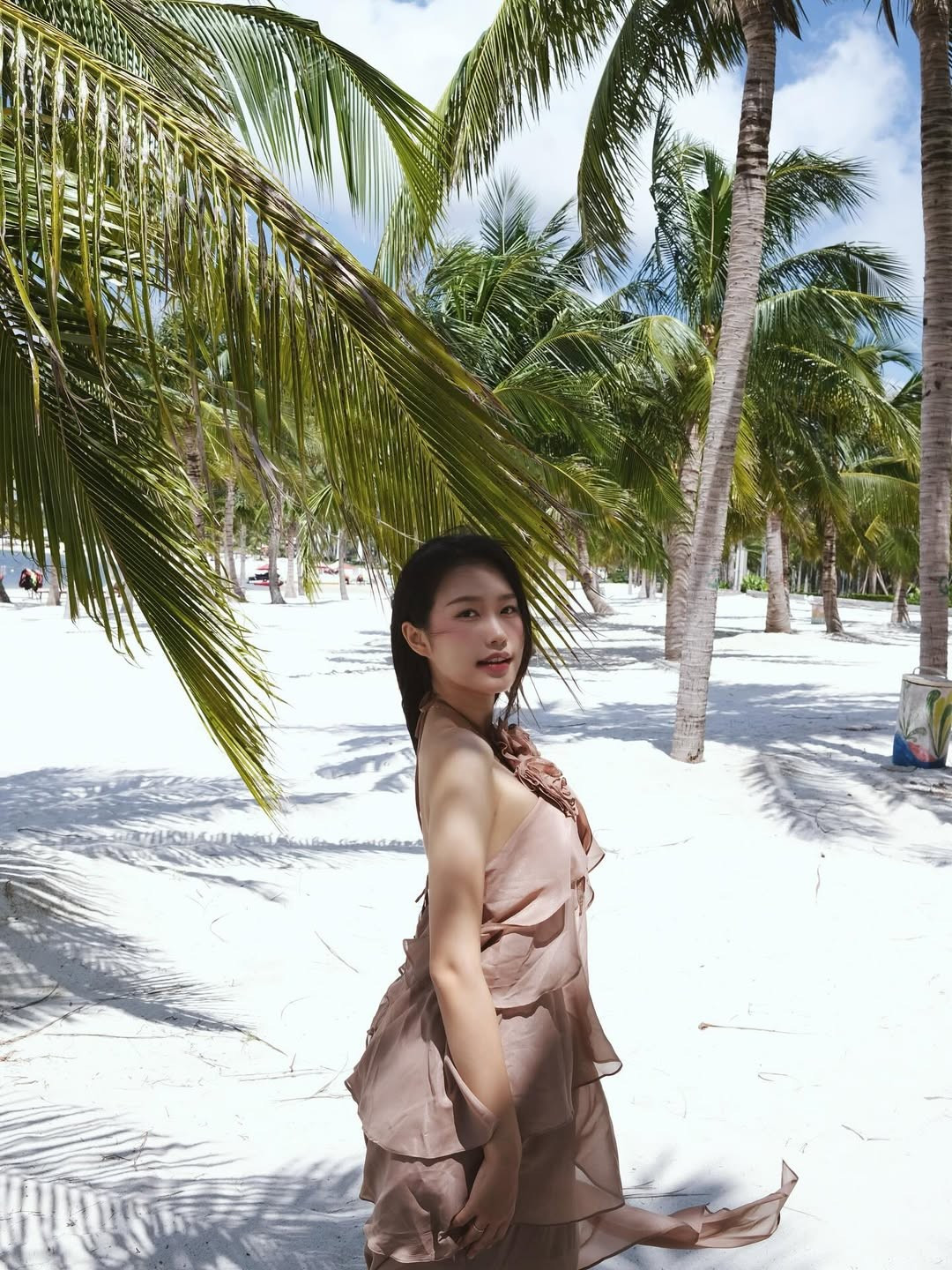 Những khoảnh khắc cô đứng giữa hàng dừa xanh mát, trên nền cát trắng mịn và biển xanh biếc, tựa như một bức tranh mùa hè hoàn hảo.