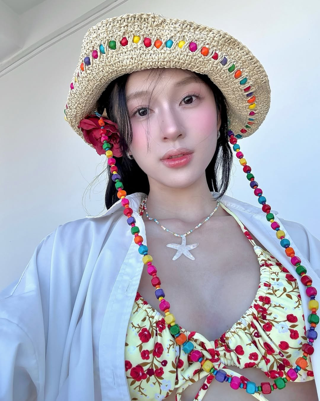 Điểm nhấn trong tạo hình là đóa hoa đỏ cài tóc – một chi tiết nhỏ nhưng giúp tổng thể trở nên mềm mại, nữ tính và đậm chất thơ giữa khung cảnh biển trời.