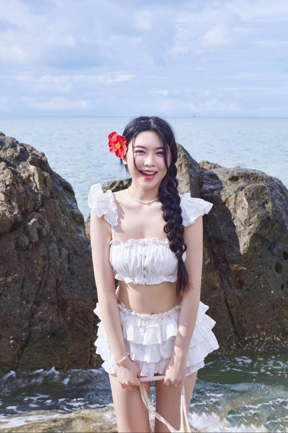 Trong loạt ảnh khác, Lọ Lem lựa chọn tông màu trắng tinh khôi với áo crop top trễ vai có chi tiết bèo nhún nữ tính. Phần chân váy tầng trắng với những lớp voan mềm mại tạo cảm giác bay bổng, nhẹ nhàng khi gió biển thổi.