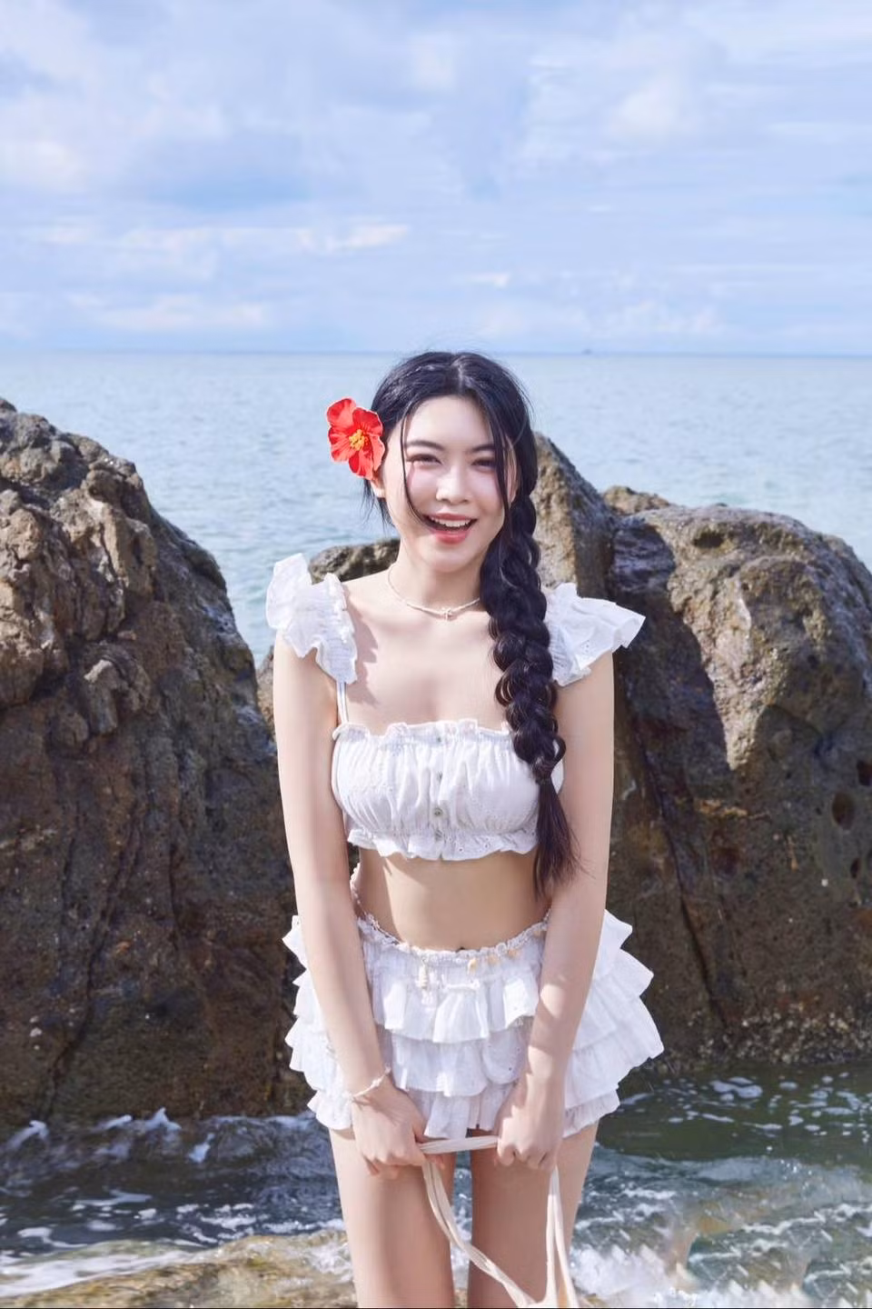 Trong loạt ảnh khác, Lọ Lem lựa chọn tông màu trắng tinh khôi với áo crop top trễ vai có chi tiết bèo nhún nữ tính. Phần chân váy tầng trắng với những lớp voan mềm mại tạo cảm giác bay bổng, nhẹ nhàng khi gió biển thổi.