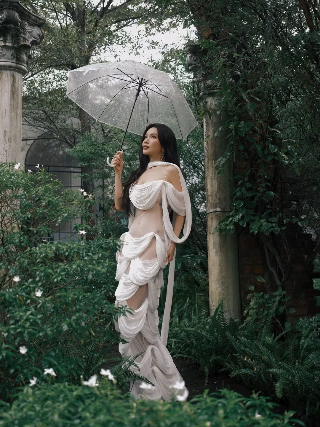 Trong những bức ảnh ngoại cảnh dưới tán cây xanh và kiến trúc cổ, Sĩ Thanh hóa thân thành nàng thơ với thiết kế váy trắng được làm từ chất liệu mỏng manh, với cách tạo khối bồng bềnh. (Ảnh: IGNV)