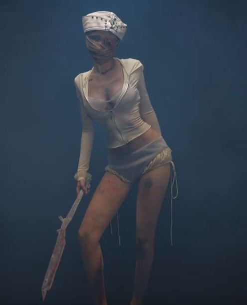 Cô nàng diện chiếc áo khoác croptop tay dài, kéo khóa hờ hững, kết hợp với quần short và mũ y tá đặc trưng, tất cả đều mang sắc trắng ngà và loang lổ như đã trải qua nhiều trận chiến kinh hoàng. (Ảnh: IGNV)